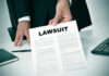 Federal Lawsuit Challenges Meta’s AI-Based Layoff Process Person holding a document titled LAWSUIT in office.