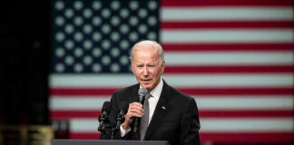 Man speaking at podium with US flag background.