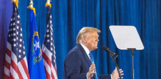 Person speaking at podium with flags in background.