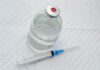 Vial of clear liquid with syringe on a white surface