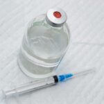 Vial of clear liquid with syringe on a white surface
