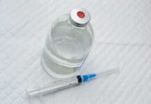 Vial of clear liquid with syringe on a white surface
