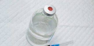 Vial of clear liquid with syringe on a white surface