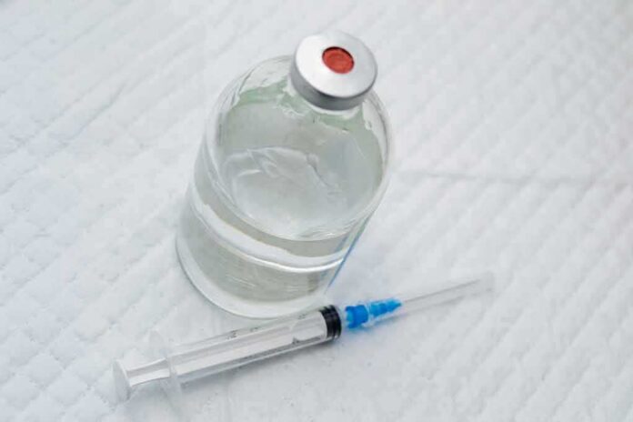 Vial of clear liquid with syringe on a white surface