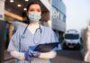 Healthcare worker in scrubs wearing mask and gloves holding a clipboard