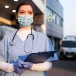 ICE Detains Maine Nurse, Sparking Hospital Protest Healthcare worker in scrubs wearing mask and gloves holding a clipboard