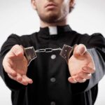 Person in black robe holding handcuffs forward