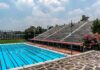 Olympic-size outdoor swimming pool beside empty stadium bleachers