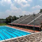 Olympic-size outdoor swimming pool beside empty stadium bleachers