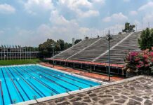 Olympic-size outdoor swimming pool beside empty stadium bleachers