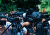 TV news cameras crowding together at an outdoor event