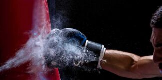 Boxer’s gloved fist strikes a red punching bag, sending chalk dust into the air