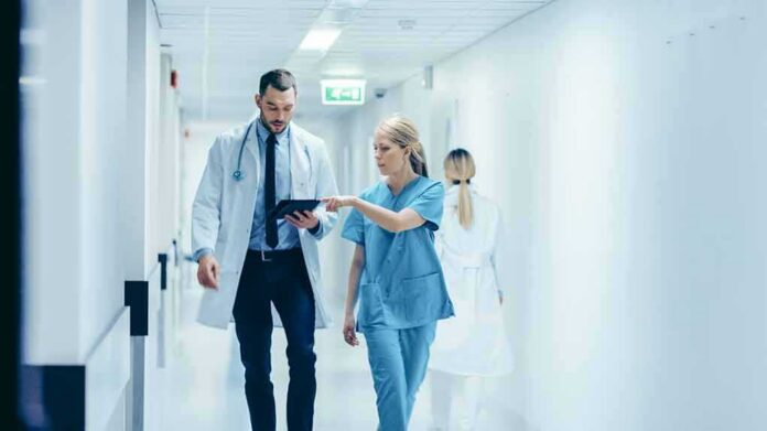 Doctor and nurse walking in a hospital corridor reviewing a tablet