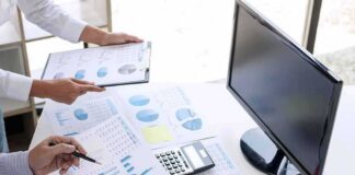 Business hands reviewing charts with a calculator and monitor on desk