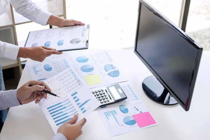 Business hands reviewing charts with a calculator and monitor on desk