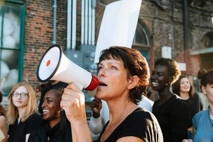 shutterstock_1250469094 Woman with megaphone speaking at a street protest