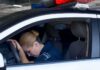 Police officer resting head on steering wheel inside patrol car