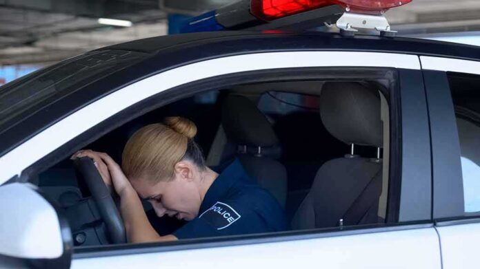 shutterstock_1492492856 Police officer resting head on steering wheel inside patrol car