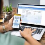 Online Betting Surges as Gen Z Takes the Lead Person using smartphone to approve bank transfer beside laptop with online banking