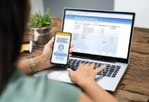 Person using smartphone to approve bank transfer beside laptop with online banking