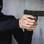 Person in balaclava aiming a handgun