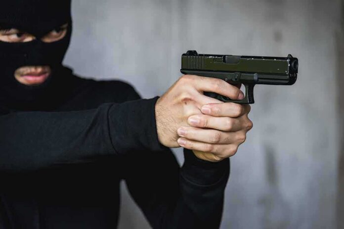 shutterstock_1738702910 Person in balaclava aiming a handgun
