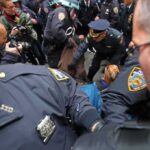 Police officers detain a person amid a crowded street scene