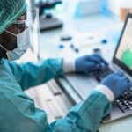 Healthcare worker in PPE using a laptop in a lab