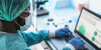 Healthcare worker in PPE using a laptop in a lab