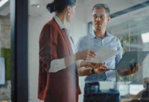 Robotics Startup Lands AI Leader Two colleagues discussing documents in a glass-walled office
