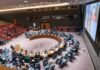 Delegates seated around a circular conference table in a large chamber