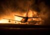 Airplane on runway with large fire and smoke at night