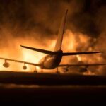 Airplane on runway with large fire and smoke at night