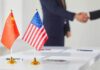 Chinese and American flags on a table with a handshake in the background
