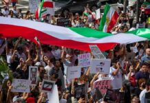 Trump Claims 100,000 Iran Protest Deaths Crowd of protesters holding signs and a large tricolor flag