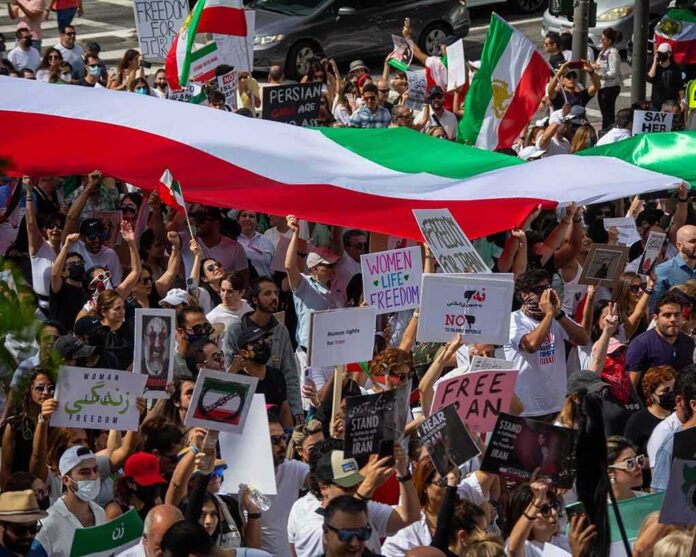 shutterstock_2208976937-1 Crowd of protesters holding signs and a large tricolor flag