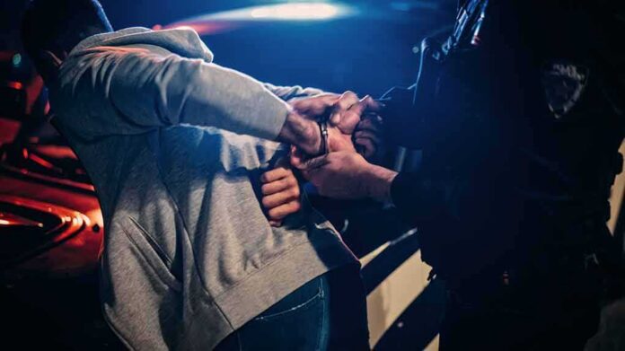 Police officer handcuffing person at night by patrol car