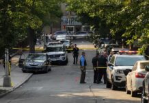Two Suspects Arrested in Fatal Attack on Musician’s Family Police officers secure a residential street with patrol cars and yellow tape