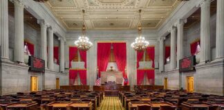 Legislative chamber with desks, chandeliers, and red curtains