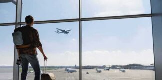 Traveler with suitcase watching plane through airport window