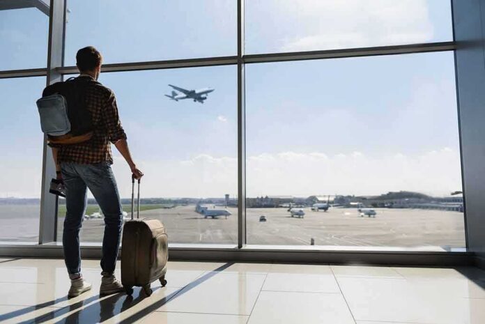 Traveler with suitcase watching plane through airport window