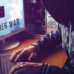 hooded person typing at a computer with multiple monitors
