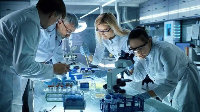 shutterstock_691541095 Scientists collaborating in a laboratory around a microscope