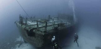 Scuba divers exploring a sunken shipwreck on the seafloor