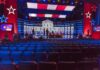 Maine Senate Race Turns to War and Wealth Debate stage with red and blue lighting and empty audience seats