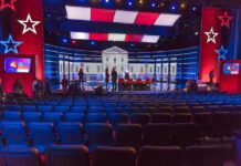 Maine Senate Race Turns to War and Wealth Debate stage with red and blue lighting and empty audience seats