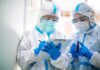 Ebola Cases Spread Across African Borders Two healthcare workers in full PPE reviewing a clipboard