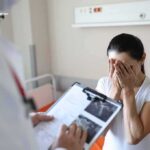 Ontario MAID Case Raises Consent Questions Woman covering her face while doctor holds a clipboard in a hospital room