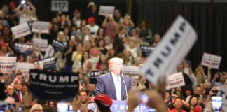 Donald Trump speaks at a rally podium as a large crowd cheers; Orel Hershiser, Ion Marin, and Billy Joe DuPree present