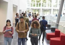 Students walking through a bright campus lobby using mobile devices
